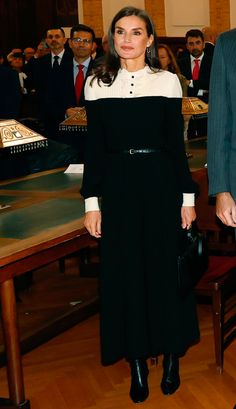 a woman in black and white dress standing next to a table with other people behind her