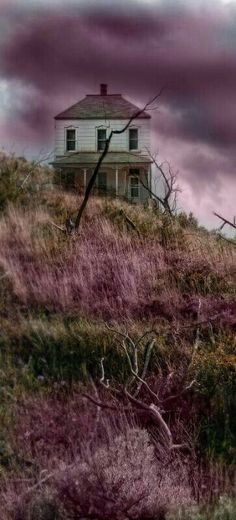 an old house sitting on top of a hill with purple clouds in the sky above