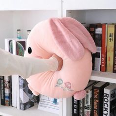 a person holding a pink stuffed animal in front of a book shelf filled with books