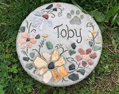 a stone with the word toy written on it and flowers painted on it in front of some grass