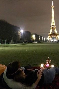 two people sitting on a blanket in front of the eiffel tower at night