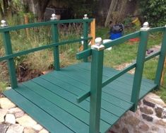 a green wooden bridge over rocks and grass