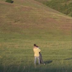 two people standing in a field with a kite flying over their heads and one person holding the other's arm