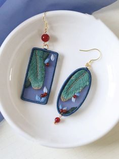 the earrings are decorated with green leaves and red beaded beads, on a white plate