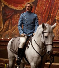 a man in uniform riding on the back of a white horse next to a painting