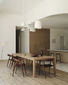 a dining room table surrounded by chairs and wooden tables with white lamps hanging from the ceiling