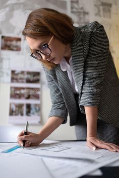 a woman in glasses is doing something on top of some papers and looking at the camera