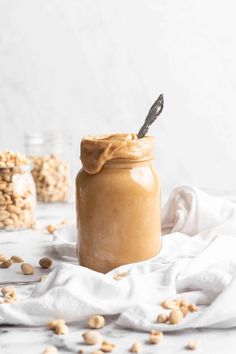 peanut butter in a glass jar with peanuts scattered around it on a white tablecloth