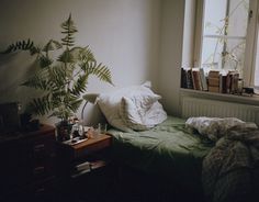 an unmade bed in a small room next to a window with books on it