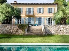 a large house sitting next to a pool in front of a lush green yard and stone wall