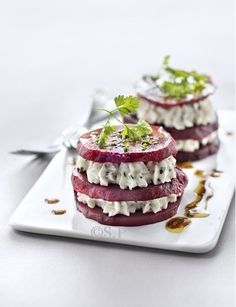 two beet sandwiches on a white plate topped with sour cream and garnish