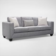 a gray couch with several pillows on the arm and backrests, in front of a white background