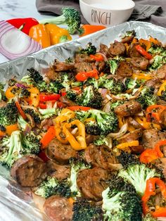 a pan filled with broccoli, peppers and meat on top of aluminum foil