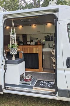 an open van door showing the kitchen and living area inside it, with plants in hanging baskets