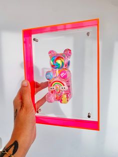 a hand is holding up a small toy in a clear box with pink trim around it