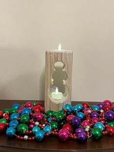 a wooden table topped with lots of christmas ornaments next to a lit candle on top of it