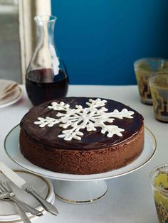 a chocolate cake with white frosting on a plate next to wine glasses and utensils