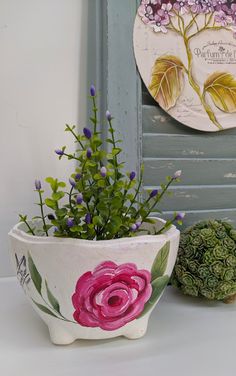 two flower pots sitting next to each other on top of a white table with purple flowers in them