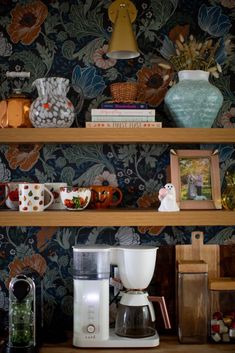 a coffee maker sitting on top of a wooden shelf next to cups and mugs