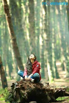 a woman sitting on top of a tree stump in the woods