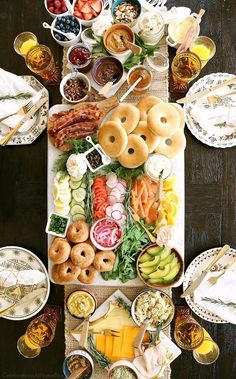 an overhead view of a table full of food and drinks, including bagels, cheeses, fruit, and other foods