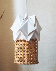 an origami bird feeder hanging from a tree branch in front of a wall