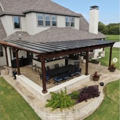 an outdoor patio with chairs and tables under a pergolated roof in front of a large house