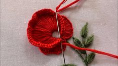 a close up of a red crochet flower on a white cloth with needles