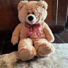 a brown teddy bear with a red bow sitting on a fur covered floor next to a wooden door