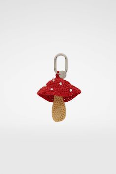 a red and white mushroom keychain hanging from a metal carabe hook on a white background