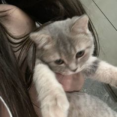 a woman holding a kitten in her arms while taking a selfie with the camera