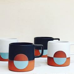 four coffee mugs sitting on top of a white table next to each other in front of a wall