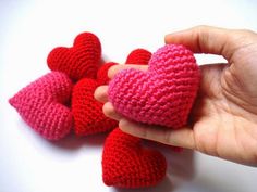 a hand is holding several small crocheted hearts in pink, red and pink