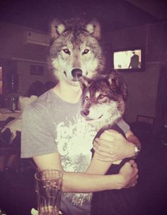 a man holding a wolf in his arms at a table with two glasses on it