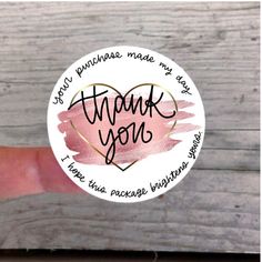 a hand holding a thank you sticker on top of a piece of wooden plank