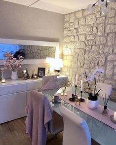 a white desk with candles and flowers on it next to a stone wall in a living room