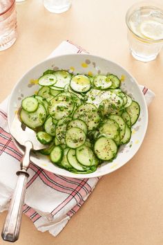 a white bowl filled with cucumbers on top of a table next to glasses