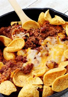 a skillet filled with chili cheese and tortilla chips on top of a wooden table