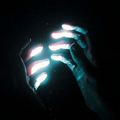 two hands holding glowing objects in the dark