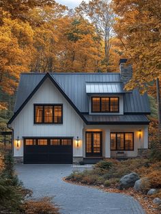 a white house with black garage doors and windows in the front yard surrounded by trees