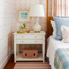 a bedroom with pink and blue wallpaper, white bedding, and a nightstand