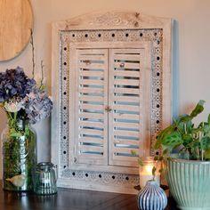 a table with vases and flowers on it in front of a white shuttered door