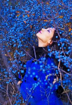 a woman with blue hair is standing among berries