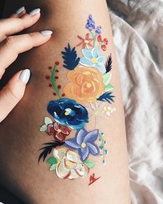 a woman's thigh with flowers painted on it and her hand holding the leg