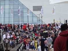 a large group of people walking down a street in front of a building with flags on it