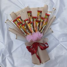 a bouquet of candy wrapped in brown paper and tied with red ribbon on top of a white sheet