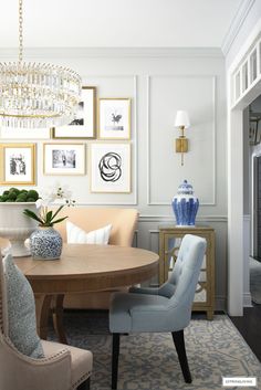 a dining room table with chairs and pictures on the wall above it, in front of a chandelier