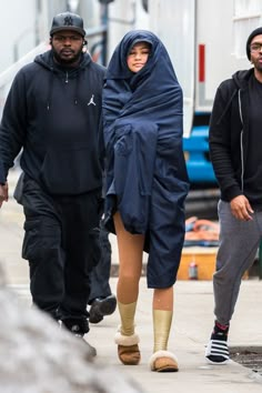 two men and a woman are walking down the street with one man wearing a hoodie