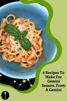 a blue bowl filled with pasta and basil on top of a green table cloth next to a