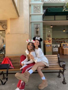 two women sitting on a bench in front of a building with mickey ears and minnie mouse hats